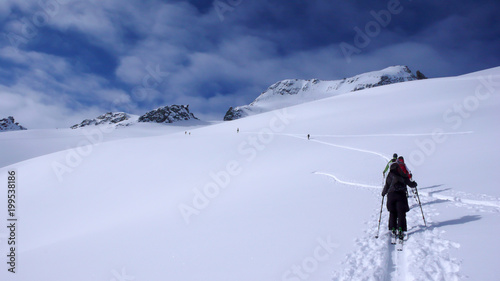 two backcountry skiers and a group of skiers ahead of them all crossing a glacier in the Alps in Austria on their way to the summit