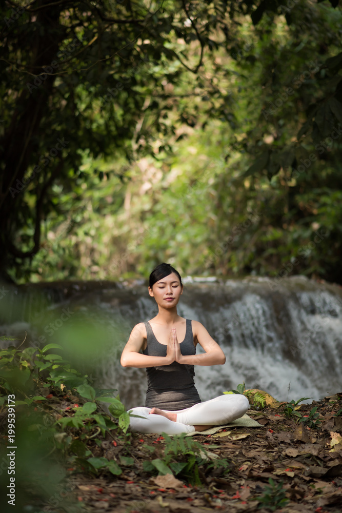 Young woman in yoga pose sitting near waterfall Young woman in yoga pose sitting near waterfall