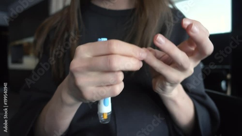 Close up of a female diabetic patient using lancelet on finger to take sample of blood sugar. Woman makes an express test for blood sugar in a restaurant public place photo