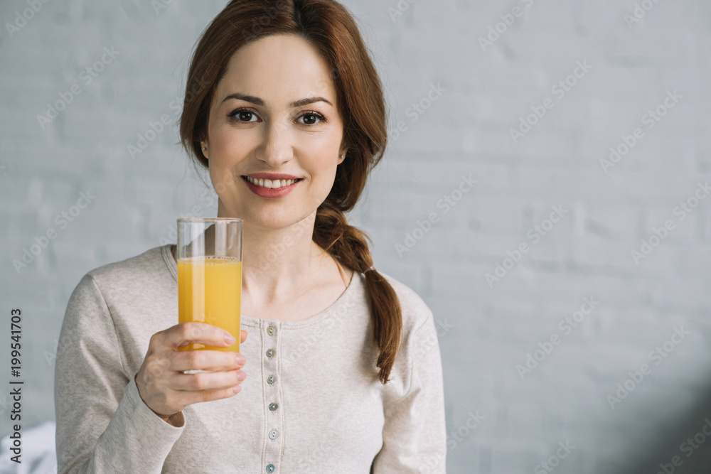 beautiful woman holding glass of orange juice and looking at camera beautiful woman holding glass of orange juice and looking at camera