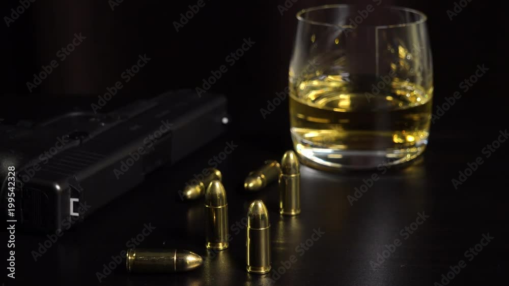 A glass of whiskey, a gun and bullets on a black table - closeup A glass of whiskey, a gun and bullets on a black table - closeup