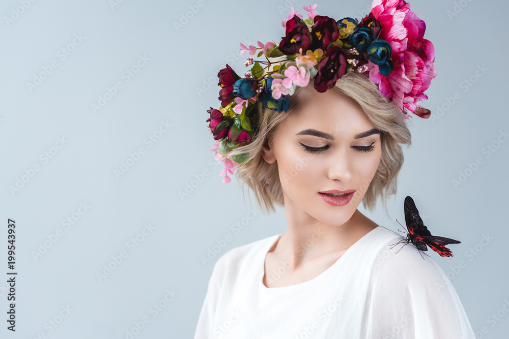 beautiful model posing in floral wreath with butterfly on shoulder, isolated on grey