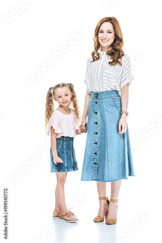 beautiful happy mother and daughter holding hands and smiling at camera isolated on white