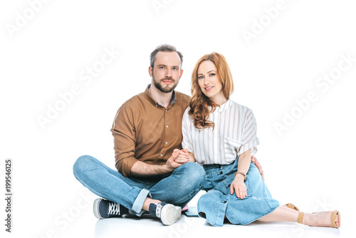 beautiful happy couple sitting together, holding hands and smiling at camera isolated on white