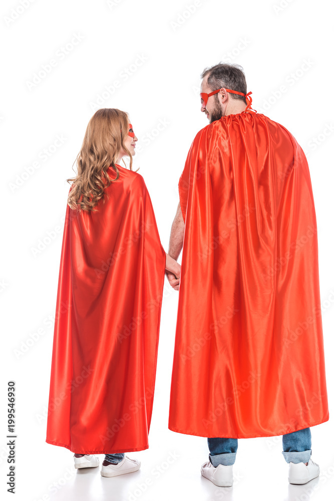 rear view of couple in masks and cloaks holding hands and looking at each other isolated on white rear view of couple in masks and cloaks holding hands and looking at each other isolated on white
