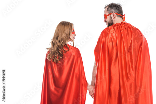 back view of super couple in masks and cloaks holding hands and looking at each other isolated on white