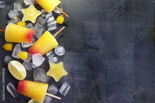 Sweet refreshing summer food concept. Summer ice cream fruit ice stars yellow orange and red colors and slices of lemon top view on dark background of table, free copy space.