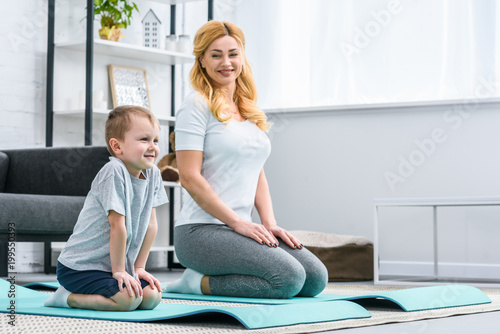 Smiling mother and son sitting on fitness mats