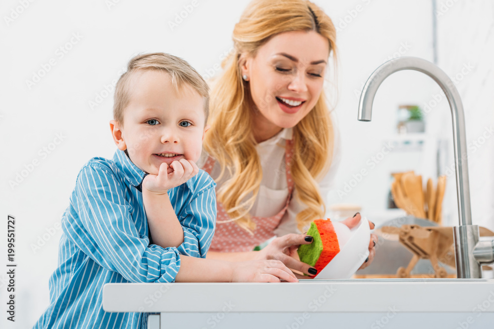 Little boy and mother washing up plate by sponge Little boy and mother washing up plate by sponge
