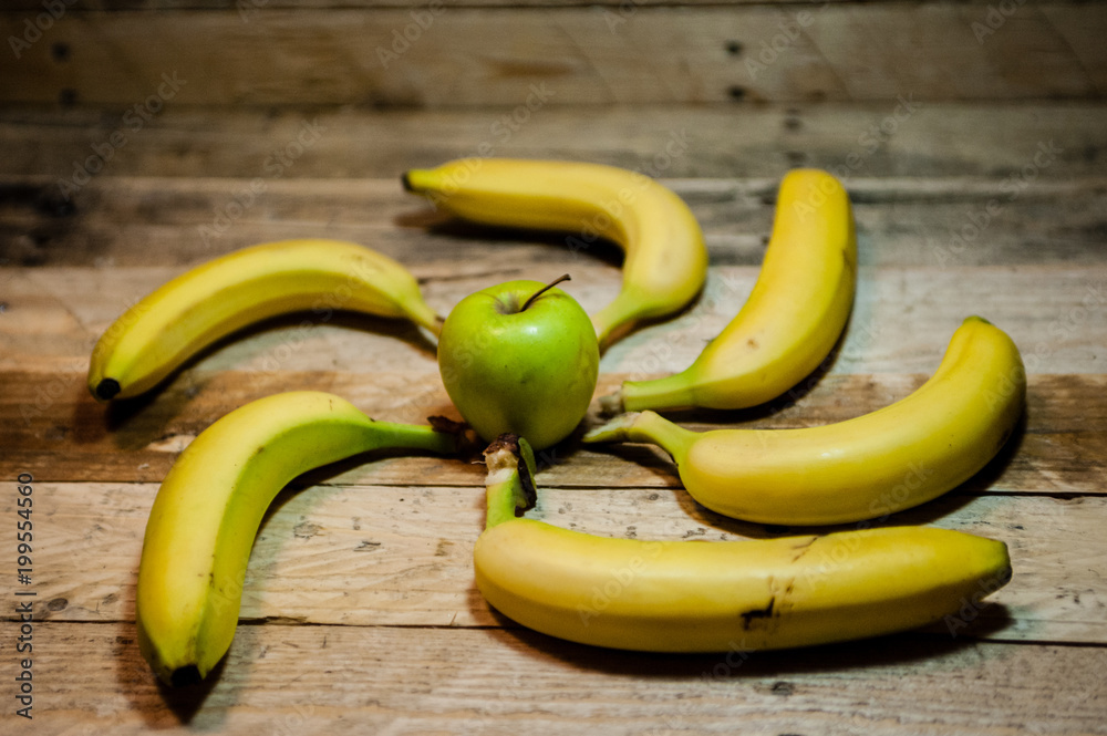 an apple in the middle with bananas around forming a wheel on rough wood background an apple in the middle with bananas around forming a wheel on rough wood background