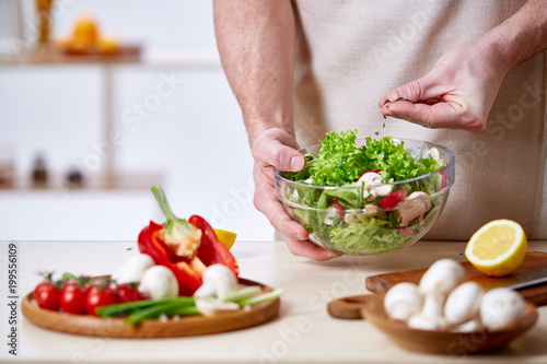 Man cooking at kitchen making healthy vegetable salad, close-up, selective focus.