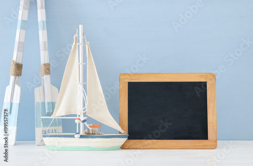 nautical concept with white decorative wooden oars and boat next to empty blackboard over blue background.
