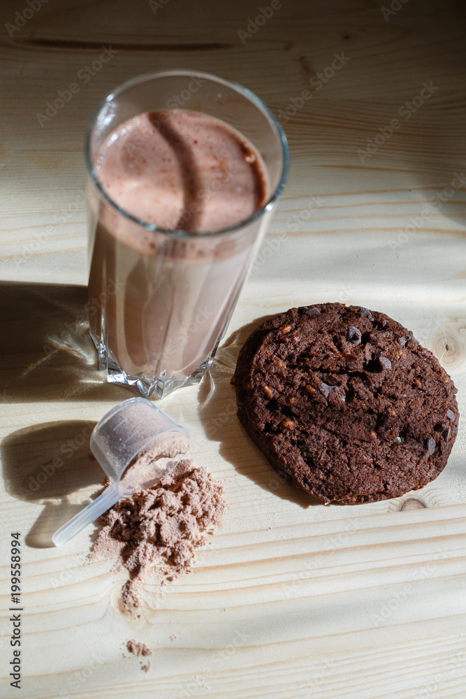 Mixed milk chocolate with whey protein shake in glass cup, scoop with  protein and chocolate cookie on wooden table. Dietary snack for  bodybuilding. Protein casein, geiner, hydrolysate after training Photos |  Adobe
