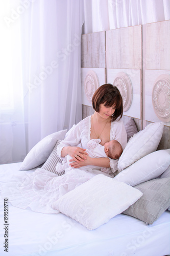 Obraz na płótnie Breastfeeding baby. Young mother holding her newborn child. Mom nursing baby. Woman and new born relax in a white bedroom. Mother breast feeding baby. w salonie
