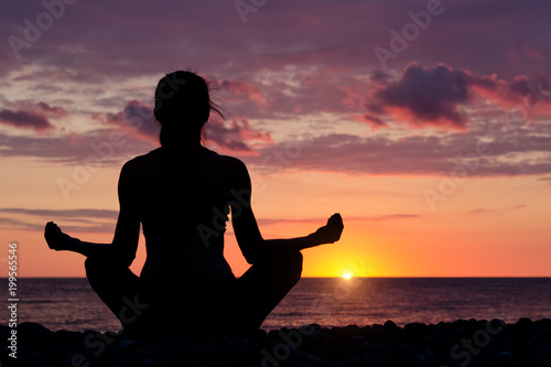 Woman meditating on the beach in lotus position. Silhouette, sunset