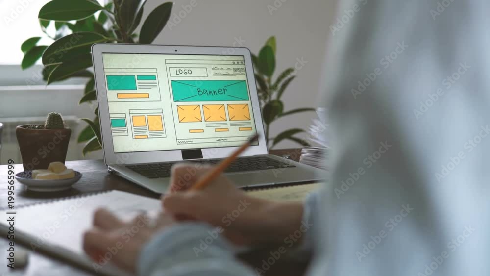 Freelancer's workplace. Web Developer makes sketches of the site in his notebook working remotely from home office