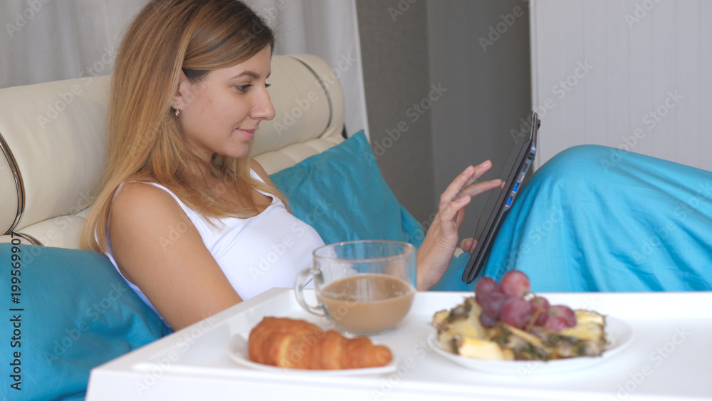 Young Woman With Laptop Eating Breakfast In Bed At Home And Drinking Coffee.