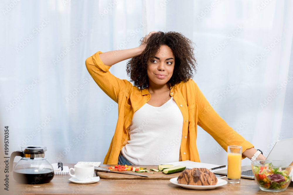 attractive young woman with various food and working supplies on table working at home attractive young woman with various food and working supplies on table working at home