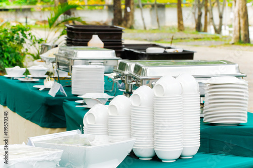 Stacked white clean plates and bowls on a light table are placed for served.