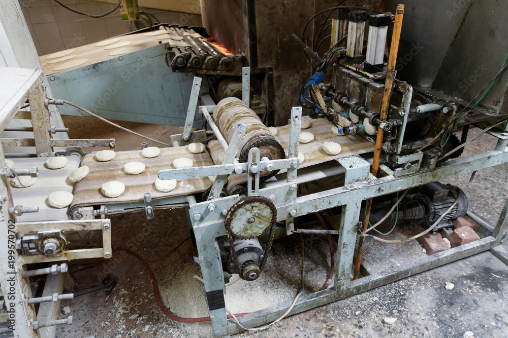 Old machine for forming dough pieces on a conveyor belt for the production of Arab flatbread in a large bakery in Aqaba, Jordan