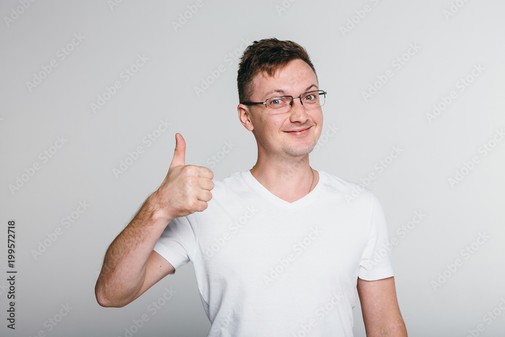 Happy successful confident man in black t-shirt showing thumbs up . Handsome young man gesturing and keeping mouth open while standing against grey background