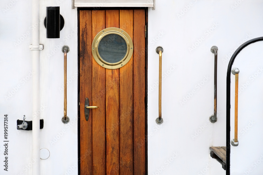 Obraz premium Vintage wooden brown door with round window on a white vessel.