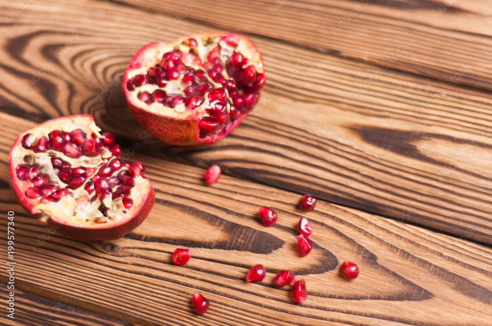 Scattered fresh ripe red seeds of pomegranate near two half pomegranate on old brown weathered wooden planks Scattered fresh ripe red seeds of pomegranate near two half pomegranate on old brown weathered wooden planks