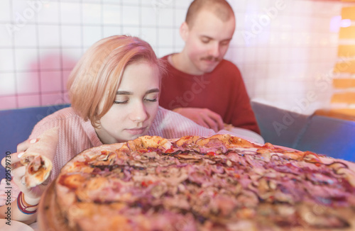 The girl smells the scent of fresh tasty pizza. Young couple sitting in a pizza near a large pizza. Delicious pizza and people