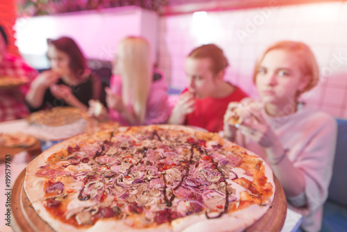A delicious large pizza in the pizzeria, against the background of a group of young people. Students eat pizza in a cozy restaurant