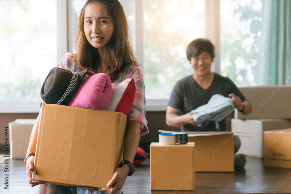 Concept young couple moving house. Asian woman holding box of stuff ready for relocation and husband is packing stuff into cardboard box prepare to move. Concept young couple moving house. Asian woman holding box of stuff ready for relocation and husband is packing stuff into cardboard box prepare to move.