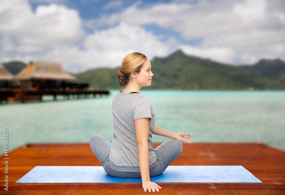 fitness, sport, people and healthy lifestyle concept - woman making yoga in twist pose on wooden pier over island beach and bungalow background