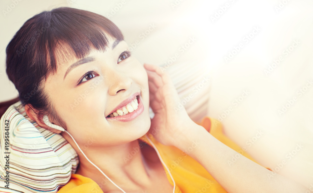 people, technology and leisure concept - happy asian young woman lying on sofa with earphones listening to music at home people, technology and leisure concept - happy asian young woman lying on sofa with earphones listening to music at home