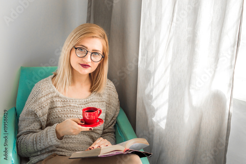 young woman reads a book in contacts and drinks coffee