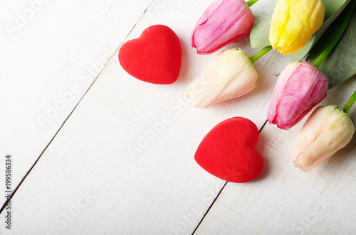 High angle shot of pink rosy and yellow Spring tulip flowers and red hearts on white wooden table