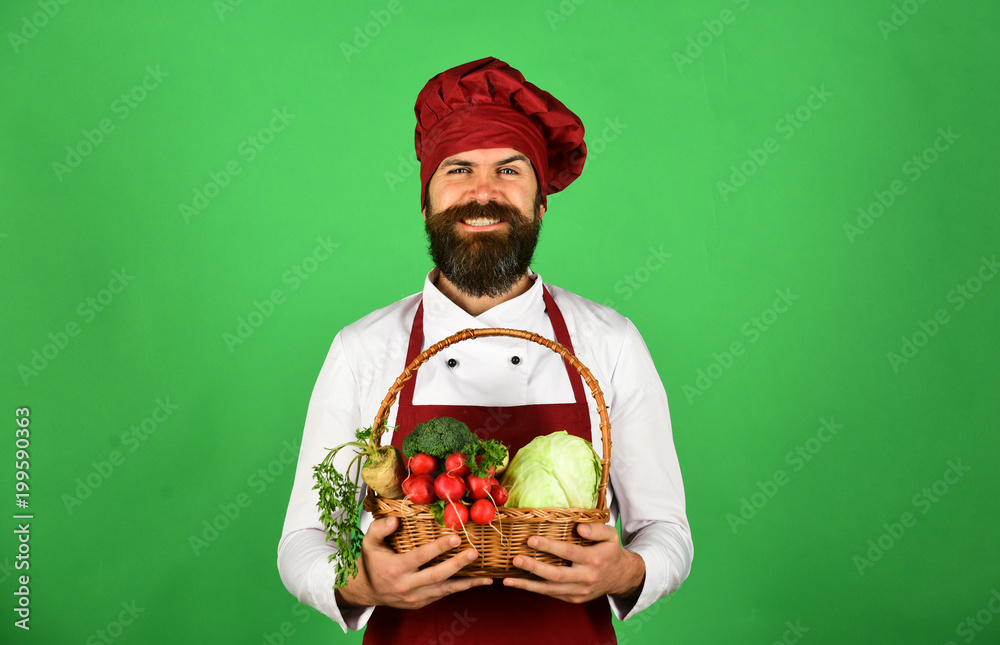 Cook with smiling face in burgundy uniform holds vegetables Cook with smiling face in burgundy uniform holds vegetables