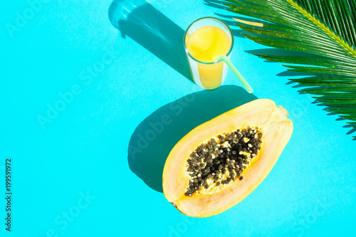 Flat Lay Arrangement Composition Tall Glass with Fresh Citrus Tropical Fruit Juice Papaya Palm Leaf on Blue Background. Harsh Midday Light Sunlight Leaks. Summer Seaside Vacation Fashion Concept photo