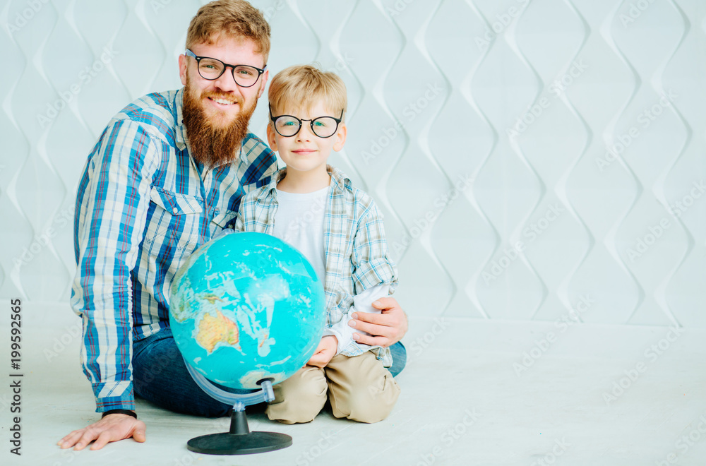 Father and son in eyeglasses looking at camera with globe at home and having fun. Full body? copy space. Father and son in eyeglasses looking at camera with globe at home and having fun. Full body? copy space.