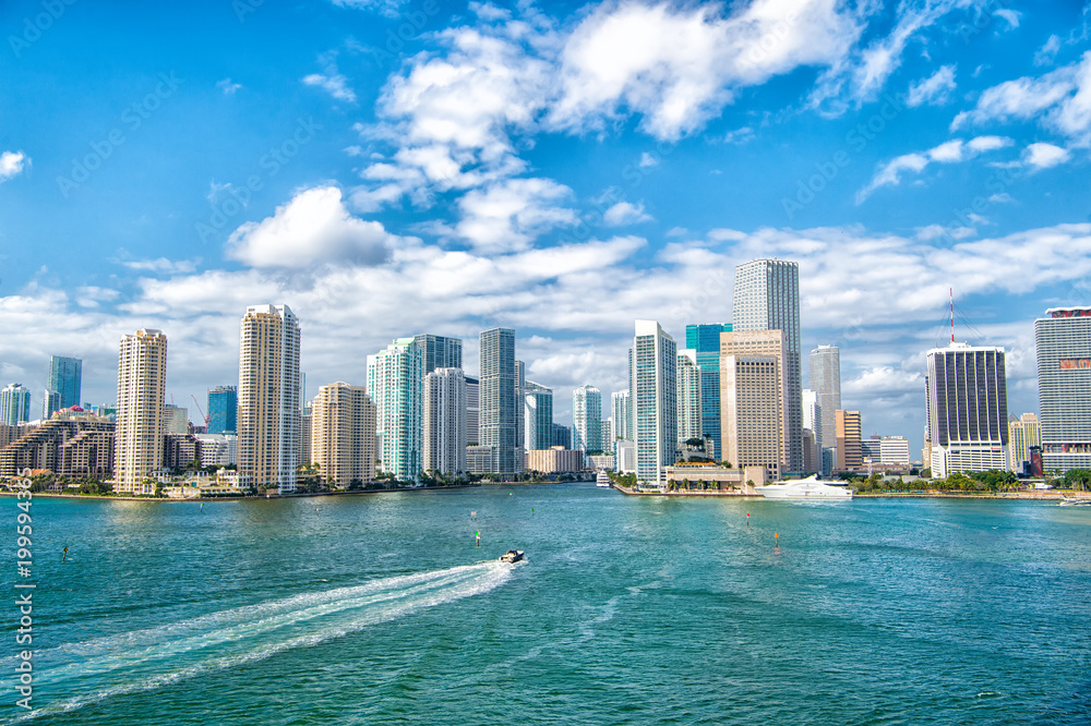 Obraz premium Widok z lotu ptaka wieżowców Miami z niebieskim pochmurnym niebem, biała łódź płynąca obok centrum Miami