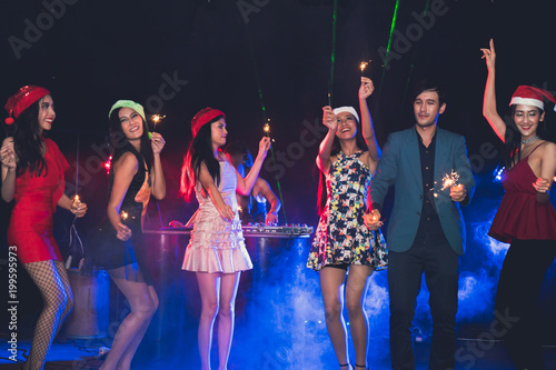 Group of young people celebrate new year party with spot light and fireworks in night party at club. selective focus on women in orange dress.