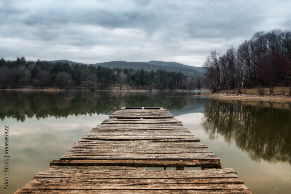 Fototapeta premium Lake pier at evening with hills on background. Reflection of the forest in the green water with blue cloudy sky. Pond at the forest. Small lake inrecreational area (Slovakia - Duchonka)