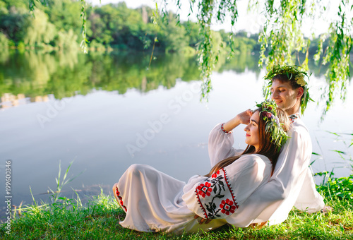 Midsummer. Young loving couple in Slavic costumes on the shore of the lake. Slavonic holiday of Ivan Kupala. photo