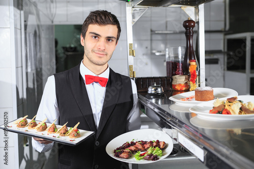 The waiter with the ready prepared dishes in the restaurant kitchen.
