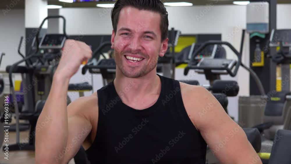 A young fit man celebrates with a smile in a gym - closeup A young fit man celebrates with a smile in a gym - closeup