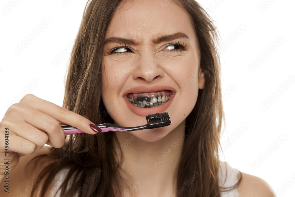 young woman brushing her teeth with a black tooth paste with active charcoal, and black tooth brush on white background young woman brushing her teeth with a black tooth paste with active charcoal, and black tooth brush on white background