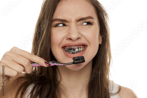 young woman brushing her teeth with a black tooth paste with active charcoal, and black tooth brush on white background photo