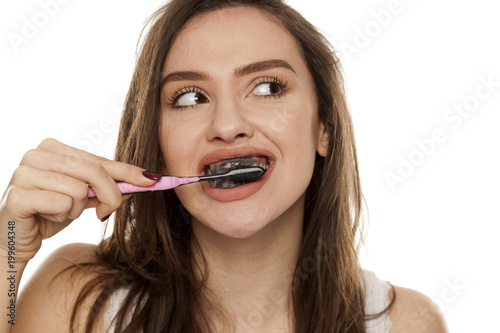 young woman brushing her teeth with a black tooth paste with active charcoal, and black tooth brush on white background