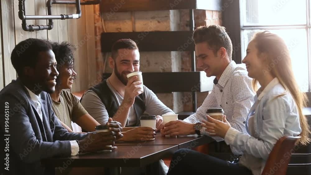 Multi-ethnic friends laughing having fun at meeting in coffeehouse, african and caucasian male buddies giving high five after telling good funny joke, multiracial young people hanging out in cozy bar