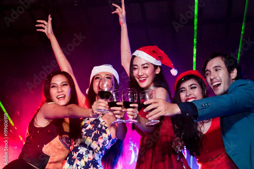 cheerful friends new year party in nightclub. Group of young people celebrate new year party throwing confetti and paper into the sky in night party at club. selective focus on woman in red hat.