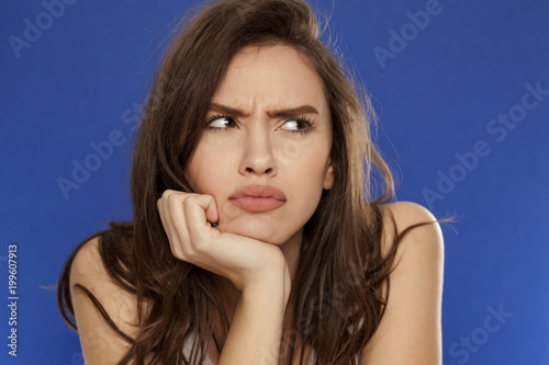 Fototapeta thoughtful young frowning woman on blue background