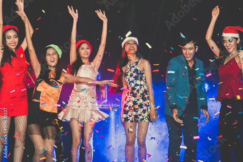 cheerful friends new year party in nightclub. Group of young people celebrate new year party throwing confetti and paper into the sky with spot light and electronic sound in night party at club.
